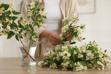 Photo of Woman making bouquet of jasmine branches at wooden table, closeup