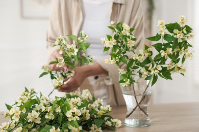 Photo of Woman making bouquet of jasmine branches at wooden table, closeup