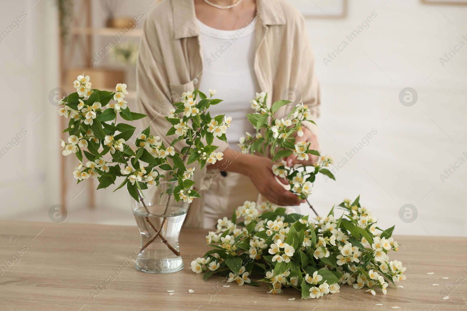 Woman making bouquet of jasmine branches at wooden table, closeup Photo of Woman making bouquet of jasmine branches at wooden table, closeup