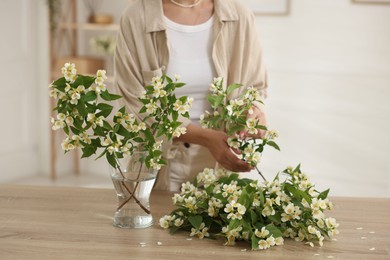 Photo of Woman making bouquet of jasmine branches at wooden table, closeup