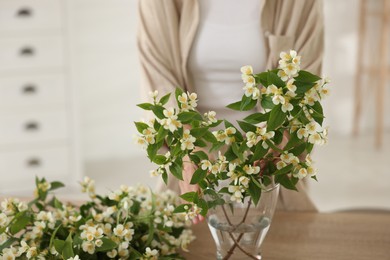 Photo of Woman making bouquet of jasmine branches at wooden table, closeup