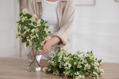 Photo of Woman making bouquet of jasmine branches at wooden table, closeup
