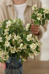 Photo of Woman making bouquet of jasmine branches at wooden table, closeup