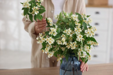 Photo of Woman making bouquet of jasmine branches at wooden table, closeup