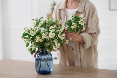 Photo of Woman making bouquet of jasmine branches at wooden table, closeup