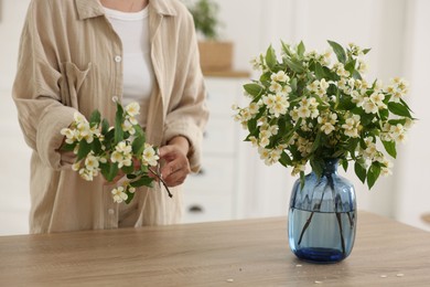 Photo of Woman making bouquet of jasmine branches at wooden table, closeup