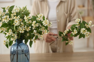 Photo of Woman making bouquet of jasmine branches at wooden table, closeup