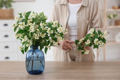 Photo of Woman making bouquet of jasmine branches at wooden table, closeup