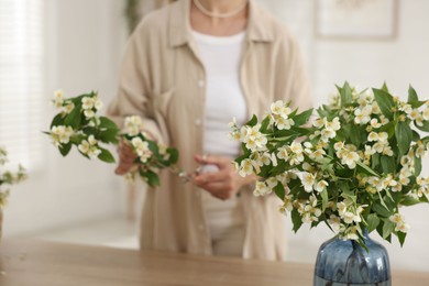 Photo of Woman making bouquet of jasmine branches at wooden table, closeup