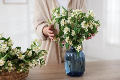 Photo of Woman making bouquet of jasmine branches at wooden table, closeup