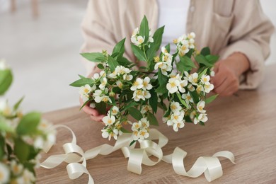 Photo of Woman making bouquet of jasmine branches at wooden table, closeup