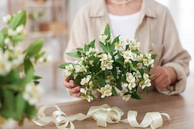 Photo of Woman making bouquet of jasmine branches at wooden table, closeup