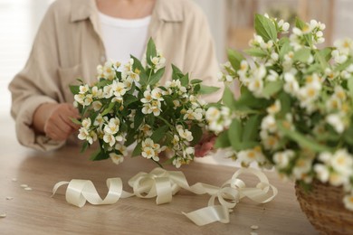 Photo of Woman making bouquet of jasmine branches at wooden table, closeup