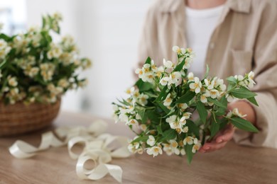 Photo of Woman making bouquet of jasmine branches at wooden table, closeup