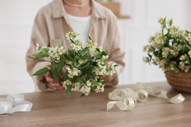 Photo of Woman making bouquet of jasmine branches at wooden table, closeup