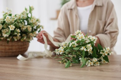 Photo of Woman making bouquet of jasmine branches at wooden table, closeup