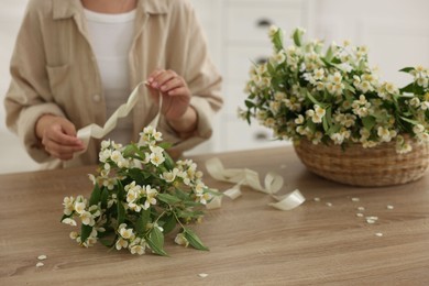 Photo of Woman making bouquet of jasmine branches at wooden table, closeup