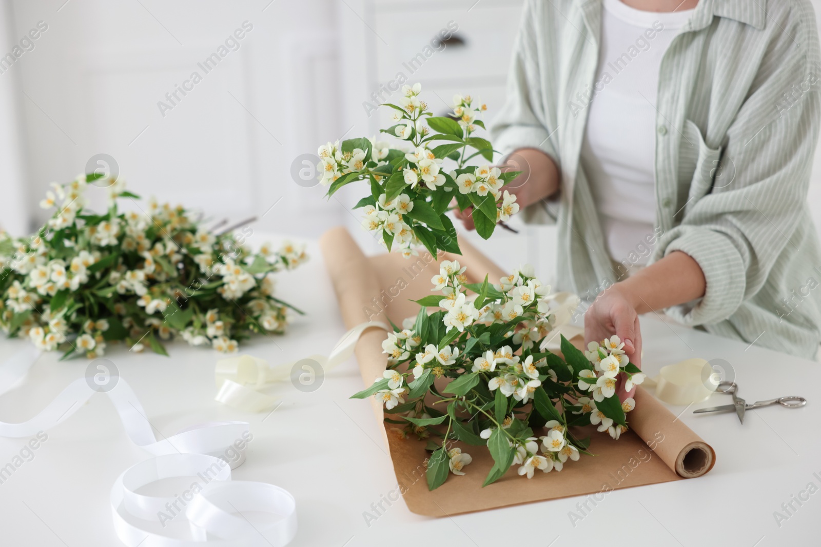 Woman making bouquet of jasmine branches at white table, closeup Photo of Woman making bouquet of jasmine branches at white table, closeup