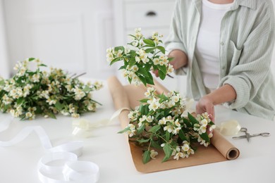 Photo of Woman making bouquet of jasmine branches at white table, closeup