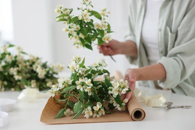Photo of Woman making bouquet of jasmine branches at white table, closeup