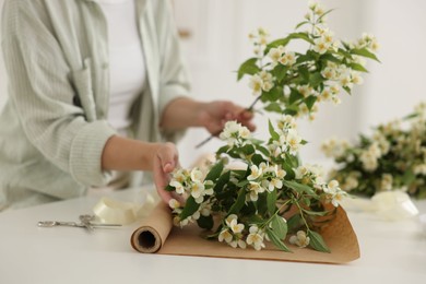 Photo of Woman making bouquet of jasmine branches at white table, closeup