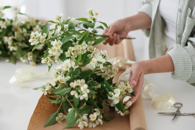 Photo of Woman making bouquet of jasmine branches at white table, closeup