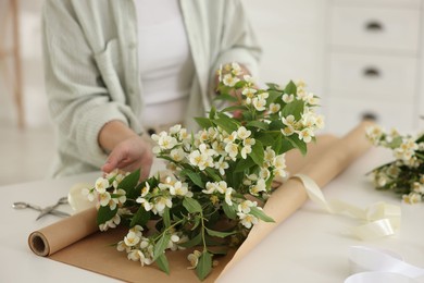 Photo of Woman making bouquet of jasmine branches at white table, closeup