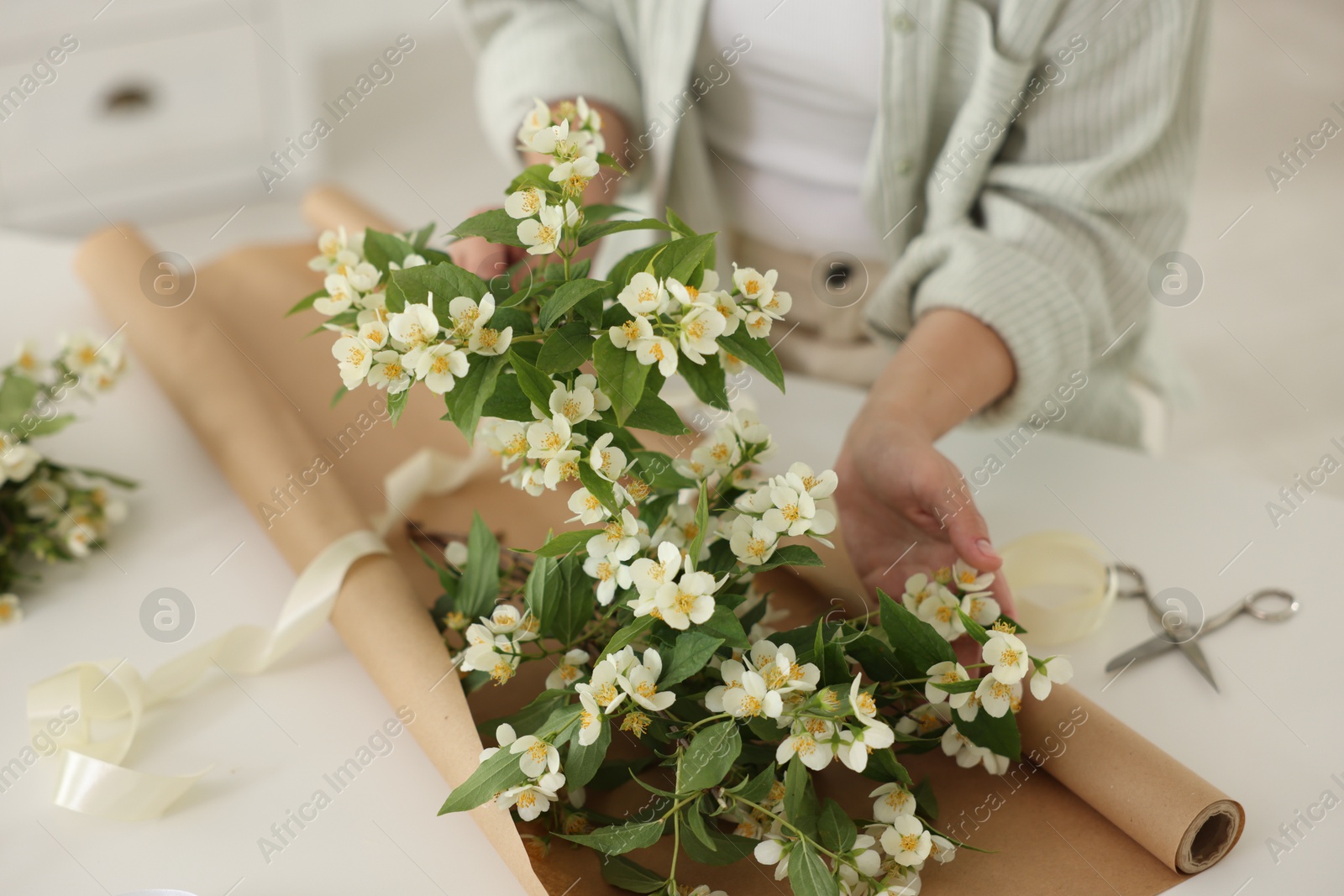 Woman making bouquet of jasmine branches at white table, closeup Photo of Woman making bouquet of jasmine branches at white table, closeup