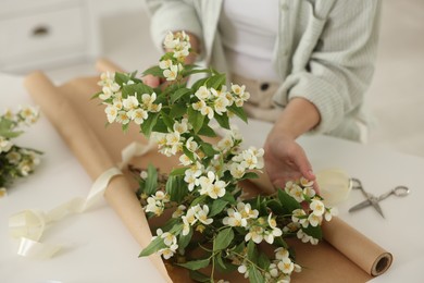 Photo of Woman making bouquet of jasmine branches at white table, closeup