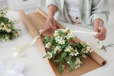 Photo of Woman making bouquet of jasmine branches at white table, closeup