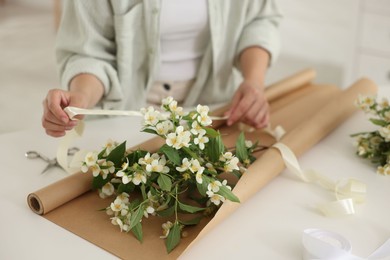 Photo of Woman making bouquet of jasmine branches at white table, closeup