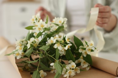 Photo of Woman making bouquet of jasmine branches at white table, closeup