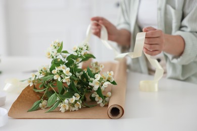 Photo of Woman making bouquet of jasmine branches at white table, closeup