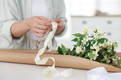 Photo of Woman making bouquet of jasmine branches at white table, closeup
