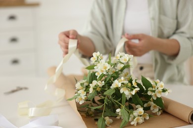 Photo of Woman making bouquet of jasmine branches at white table, closeup