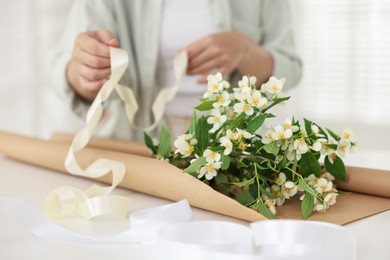 Photo of Woman making bouquet of jasmine branches at white table, closeup