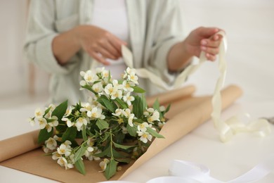 Photo of Woman making bouquet of jasmine branches at white table, closeup