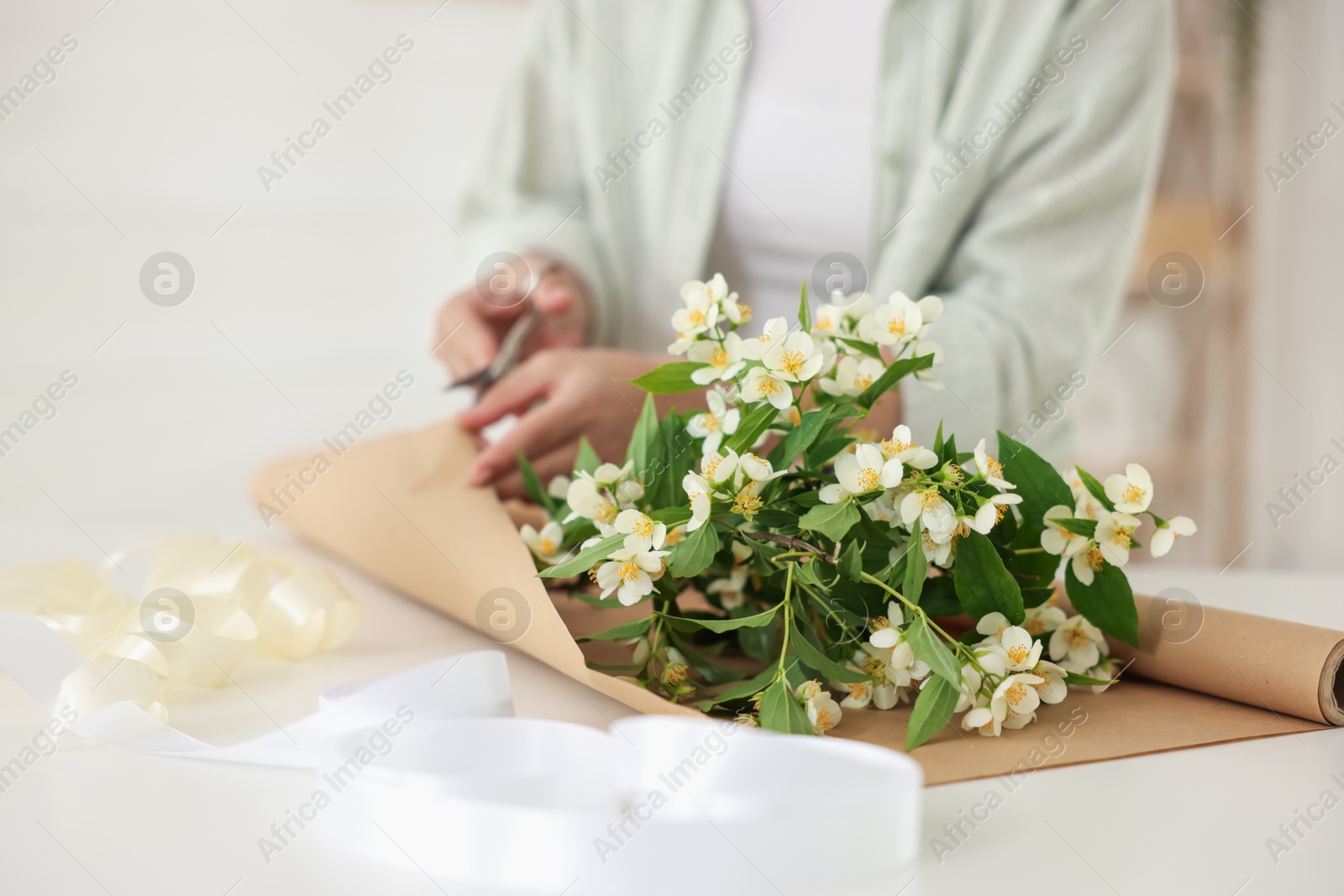 Woman making bouquet of jasmine branches at white table, closeup Photo of Woman making bouquet of jasmine branches at white table, closeup