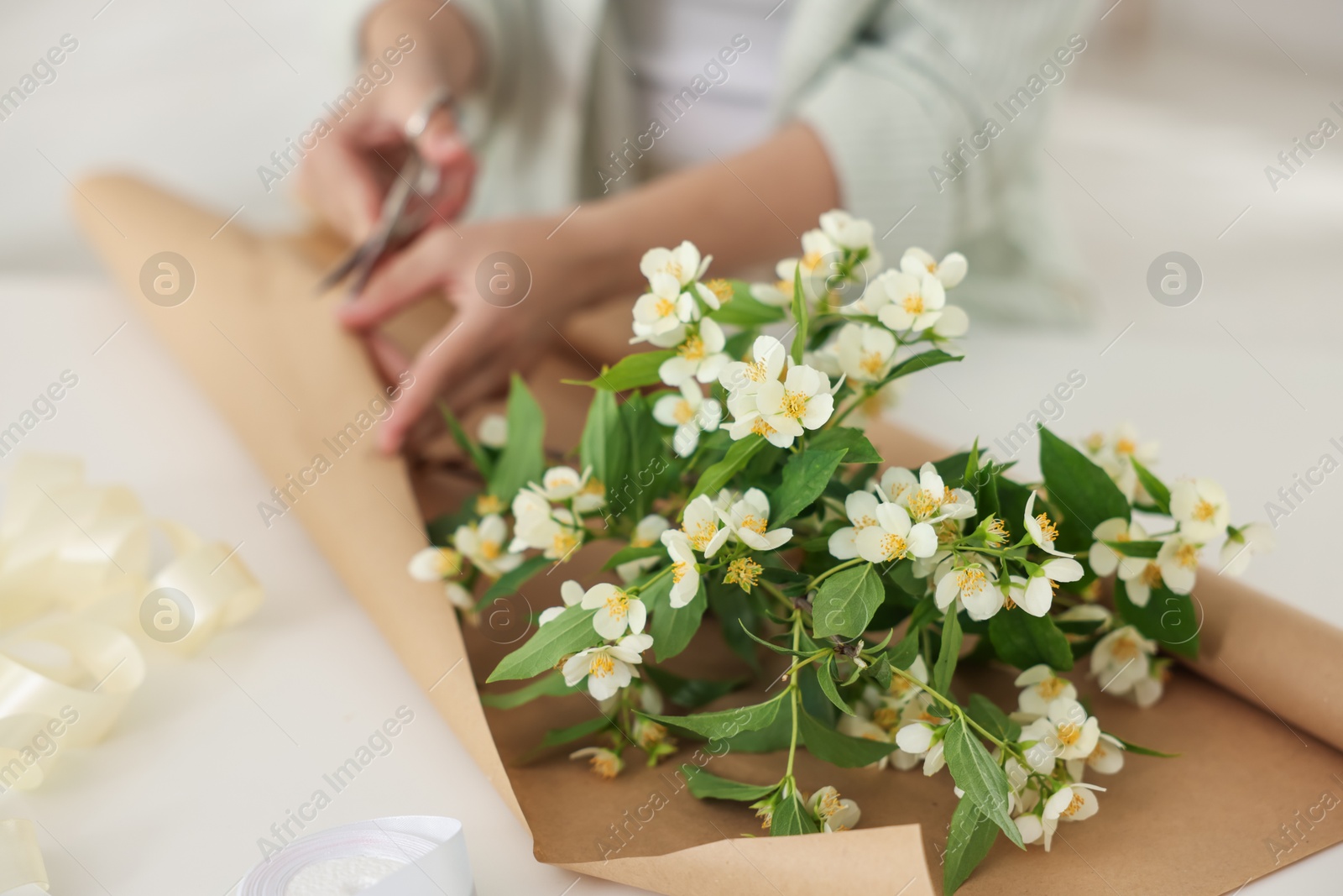 Woman making bouquet of jasmine branches at white table, closeup Photo of Woman making bouquet of jasmine branches at white table, closeup