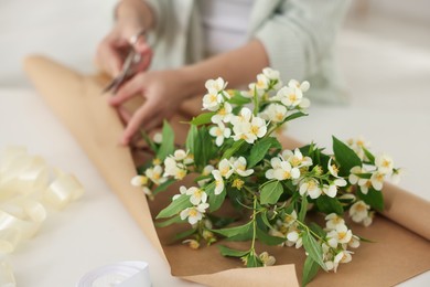 Photo of Woman making bouquet of jasmine branches at white table, closeup