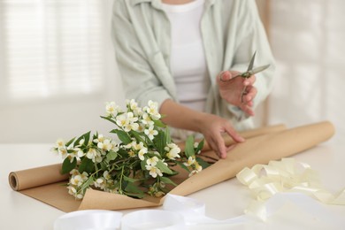 Photo of Woman making bouquet of jasmine branches at white table, closeup