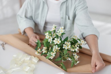 Photo of Woman making bouquet of jasmine branches at white table, closeup