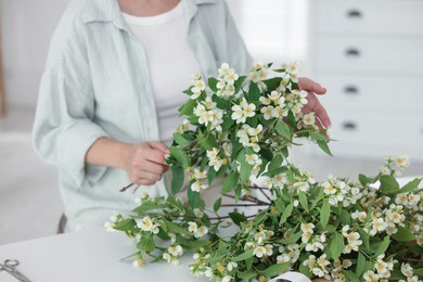 Photo of Woman making bouquet of jasmine branches at white table, closeup