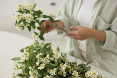 Photo of Woman making bouquet of jasmine branches at white table, closeup