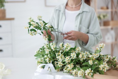 Photo of Woman making bouquet of jasmine branches at white table, closeup