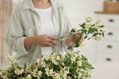 Photo of Woman making bouquet of jasmine branches at white table, closeup