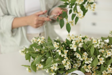 Photo of Woman making bouquet of jasmine branches at white table, closeup