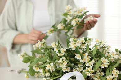 Photo of Woman making bouquet of jasmine branches at white table, closeup