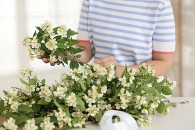 Photo of Woman making bouquet of jasmine branches at white table, closeup