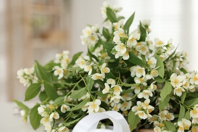 Photo of Branches with beautiful jasmine flowers and green leaves indoors, closeup